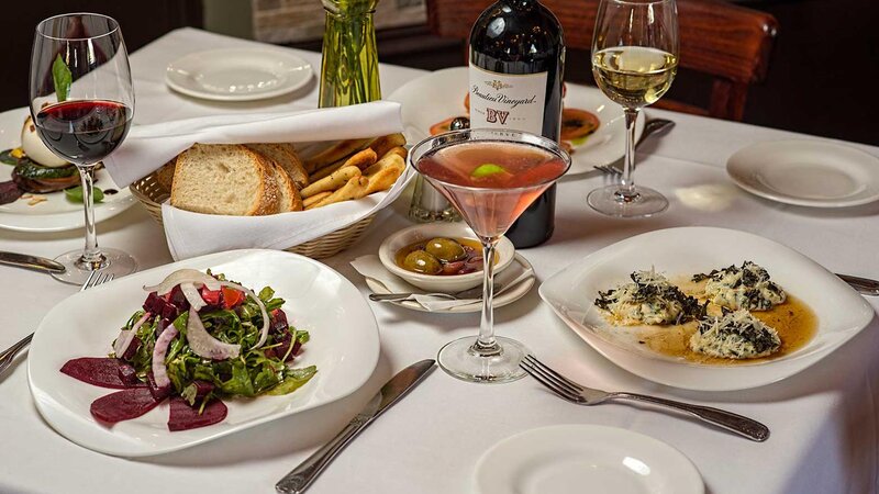 Multiple plated appetizers with rose, red and white wine and a basket of bread