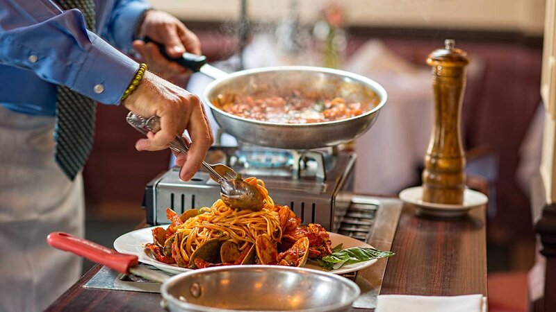 Chef topping clams and lobster being prepared tableside