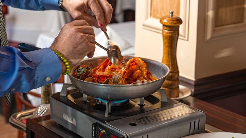 Chef preparing lobster and clams in a pan tableside